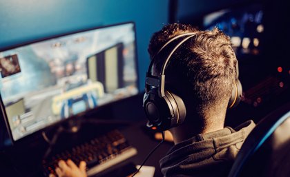 A person wearing headphones looking at a computer screen gaming 